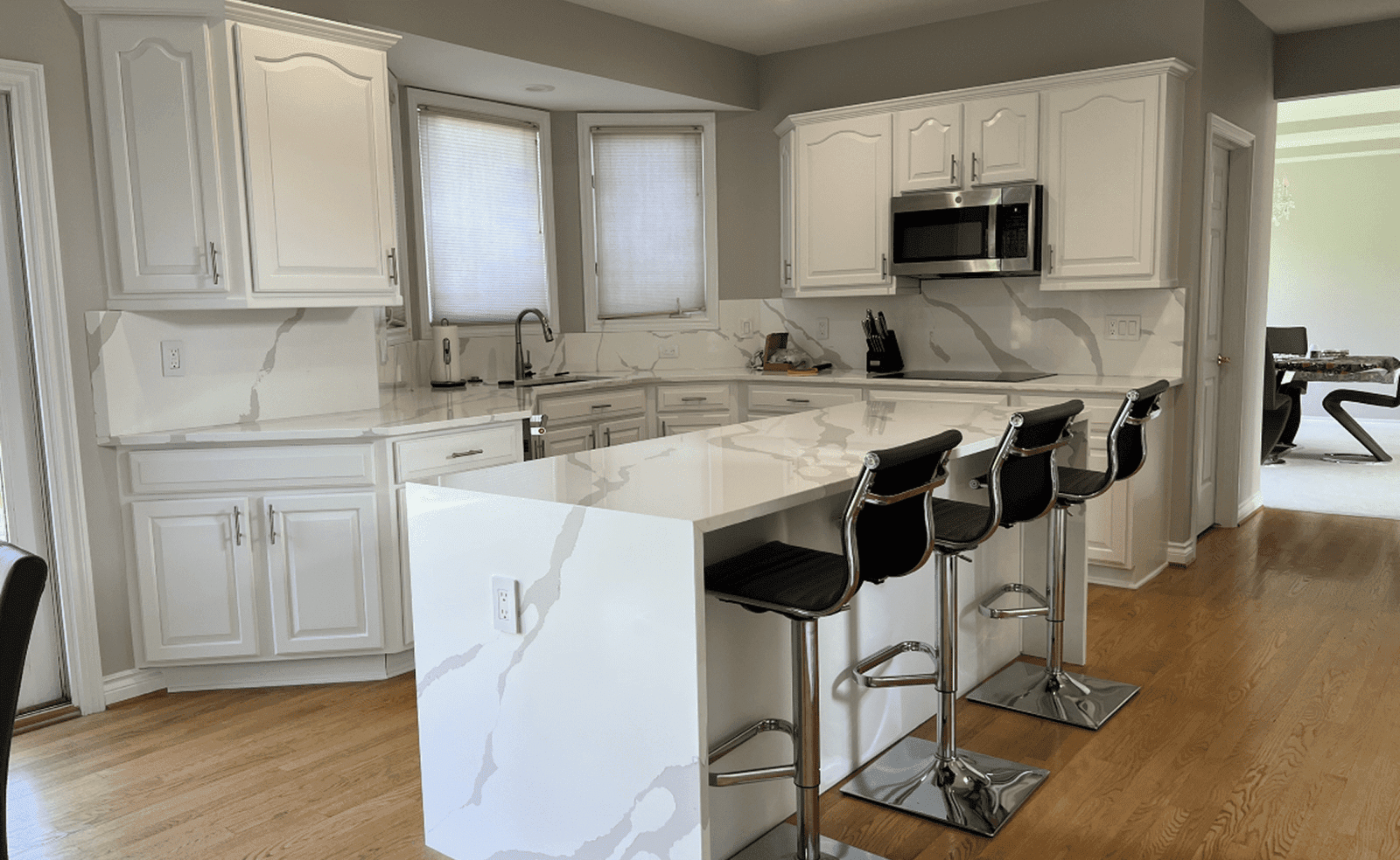 Sterling Heights, MI 13 Modern kitchen with white marble island, black bar stools, white cabinets, and stainless appliances.