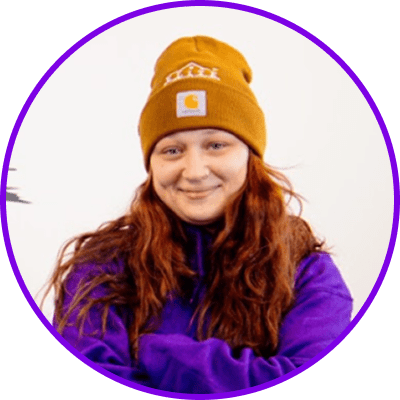 Home 21 Person with long reddish-brown hair, mustard beanie, purple sweater, on plain background, purple border.