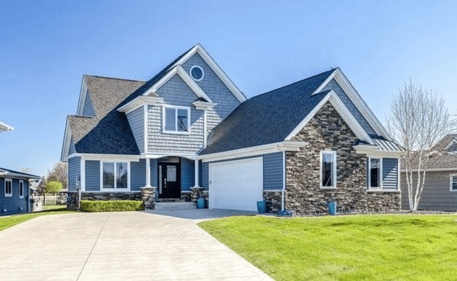 Sterling Heights, MI 12 Two-story house with gable roof, stone and siding exterior, driveway, and green yard under blue sky.